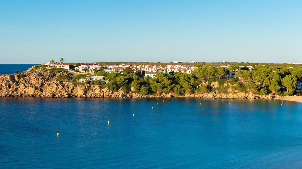 A coastal town with a rocky shoreline, a sandy beach, and buildings on a hillside.