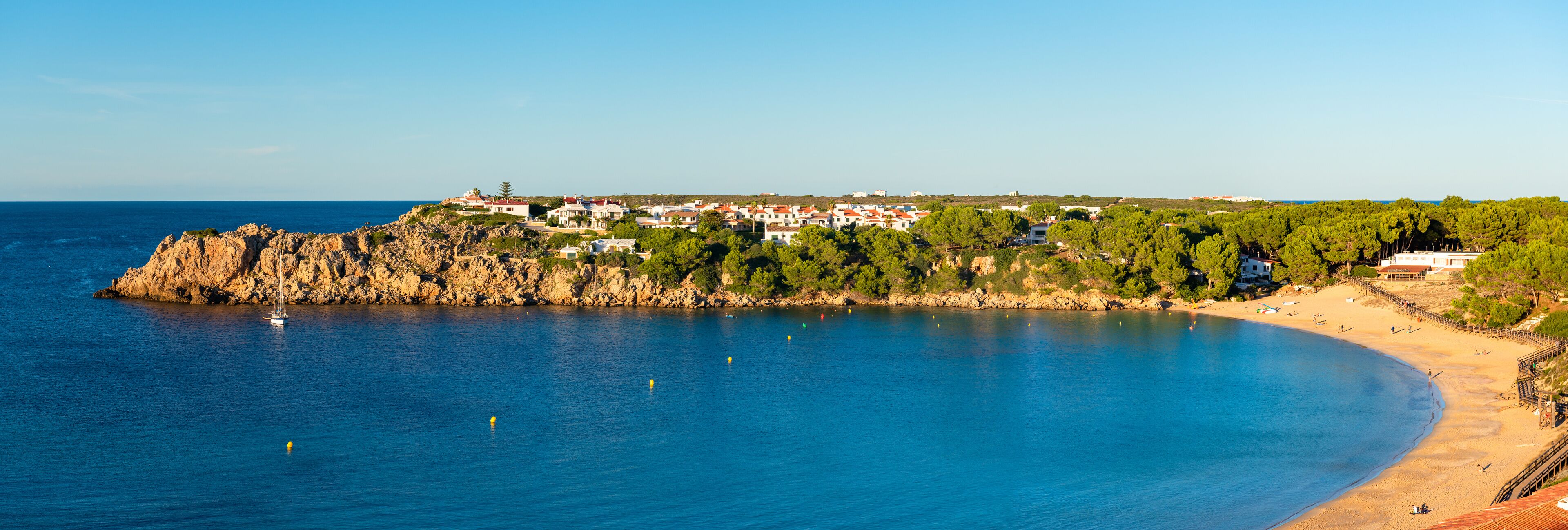 A coastal town with a rocky shoreline, a sandy beach, and buildings on a hillside.