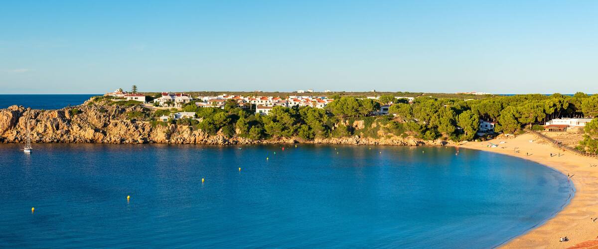 A coastal town with a rocky shoreline, a sandy beach, and buildings on a hillside.