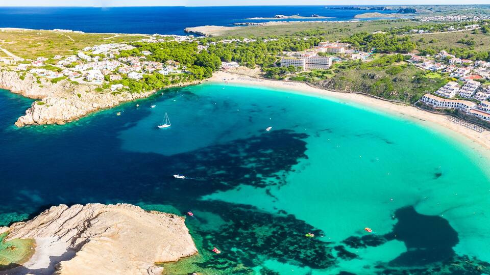 A coastal town with a beach, clear turquoise waters, and rocky outcrops.