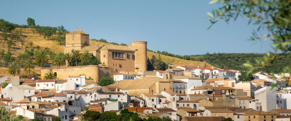 A historic town with a prominent castle on a hill, surrounded by white buildings with red-tiled roofs.