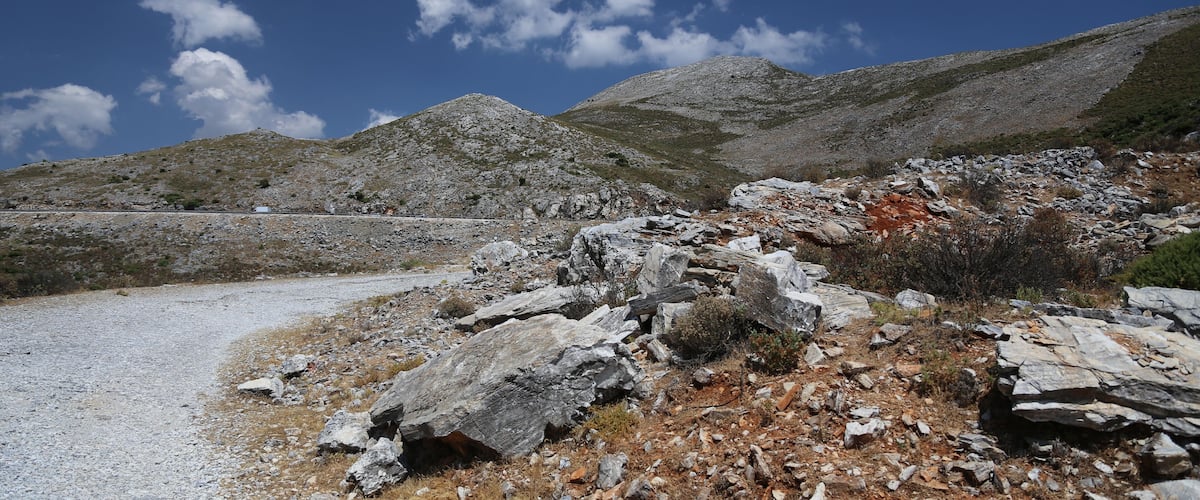 A rocky landscape with a gravel path, large boulders, and distant mountains under a clear sky.
