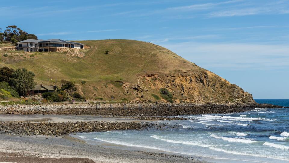 A coastal landscape with a house on a grassy hill overlooking the ocean.