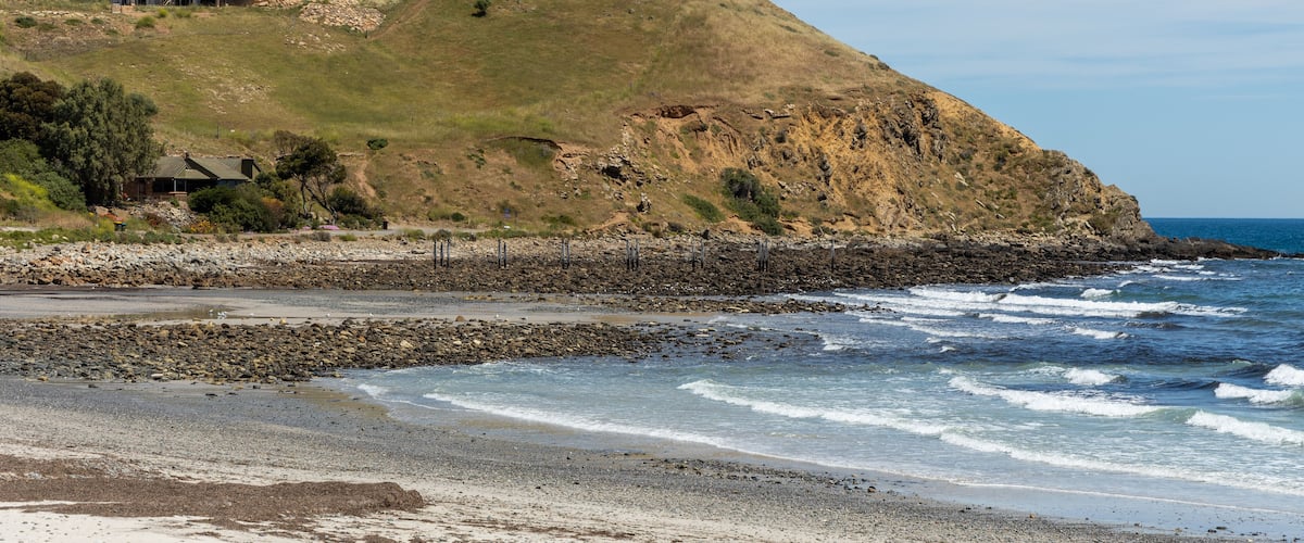 A coastal landscape with a house on a grassy hill overlooking the ocean.