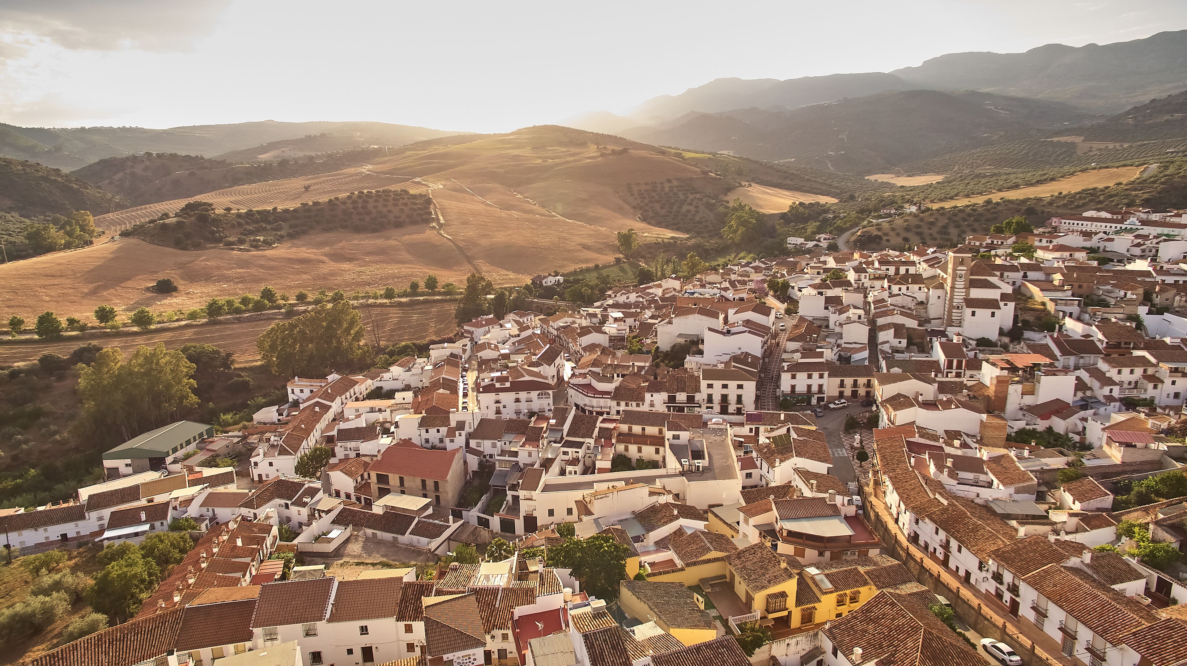 A town with white buildings and terracotta roofs nestled in a valley surrounded by hills.
