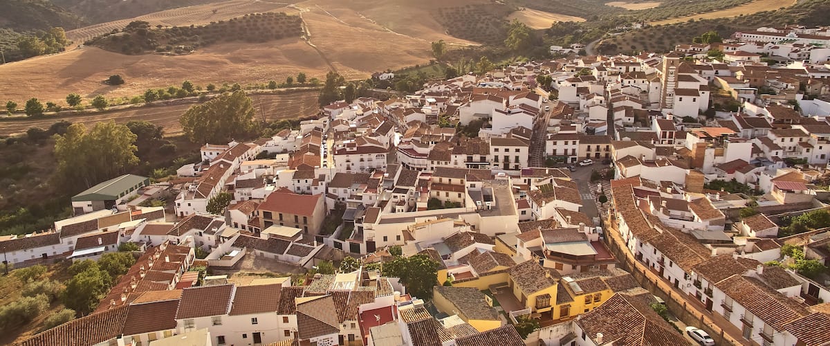 A town with white buildings and terracotta roofs nestled in a valley surrounded by hills.