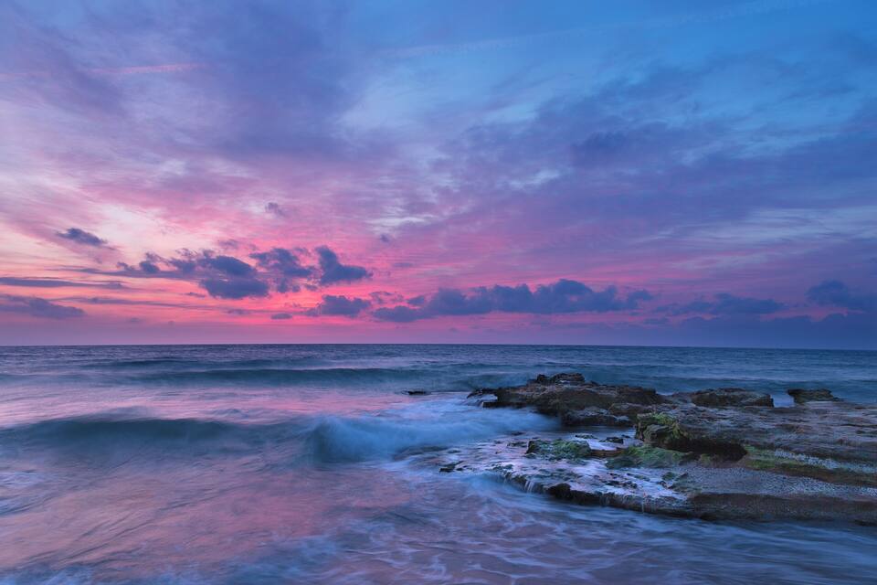 A coastal sunset with pink and purple clouds over the ocean.