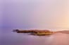 A rocky shoreline with calm water and a gradient sky.