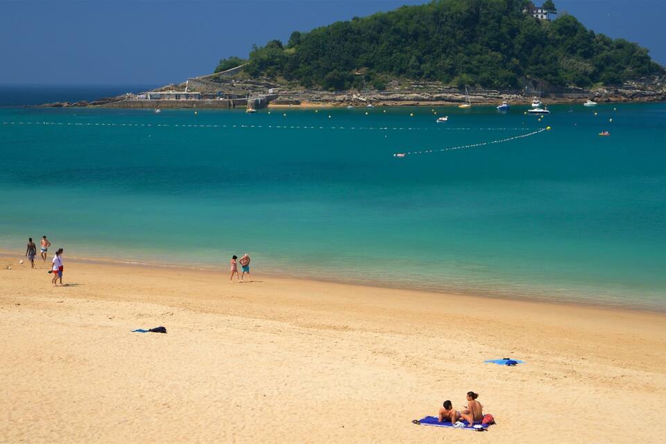 A beach with clear turquoise water, a sandy shore, and a small island with dense greenery in the background.