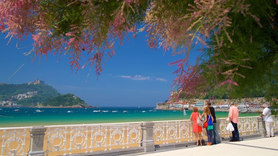 A coastal city with a clear view of the sea, a prominent hill with buildings, and a decorative railing.
