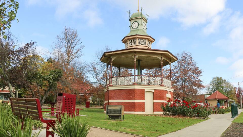 A gazebo with a clock tower, surrounded by benches and a pathway.