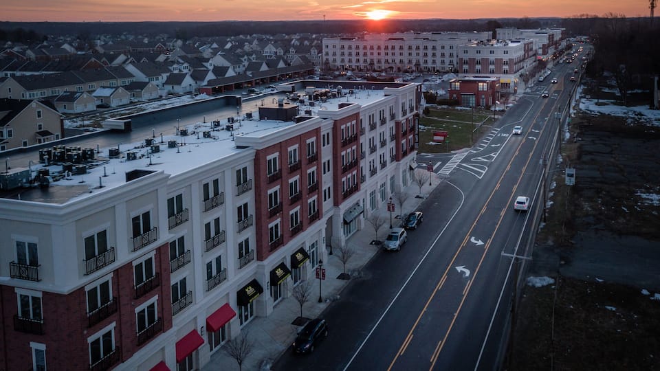 A wide street lined with multi-story buildings, a sunset in the background, and snow on the ground.
