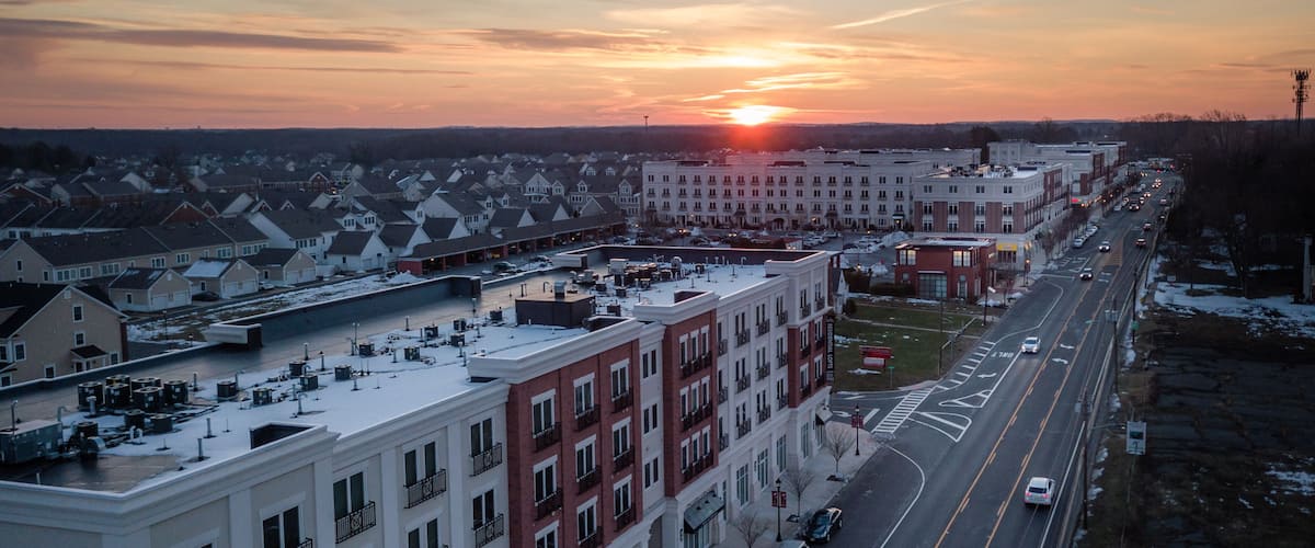 A wide street lined with multi-story buildings, a sunset in the background, and snow on the ground.