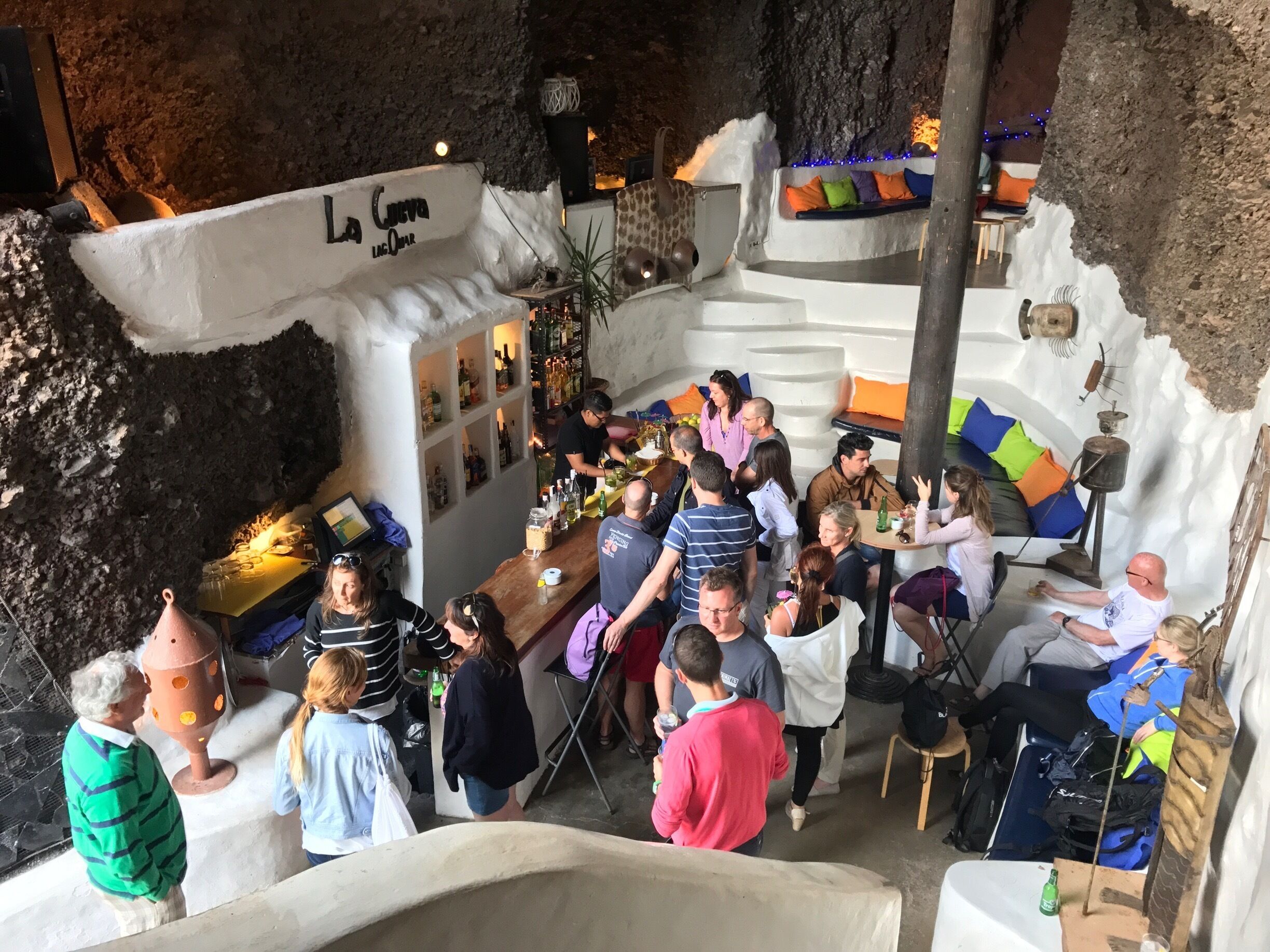 A cave bar with a rustic interior, a bar counter, and a seating area with cushions.
