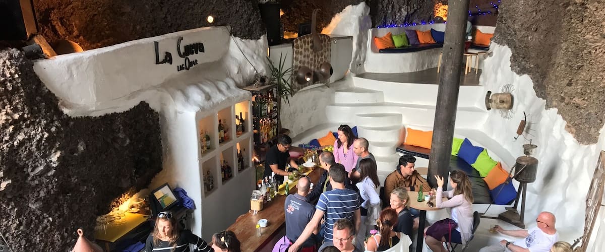 A cave bar with a rustic interior, a bar counter, and a seating area with cushions.