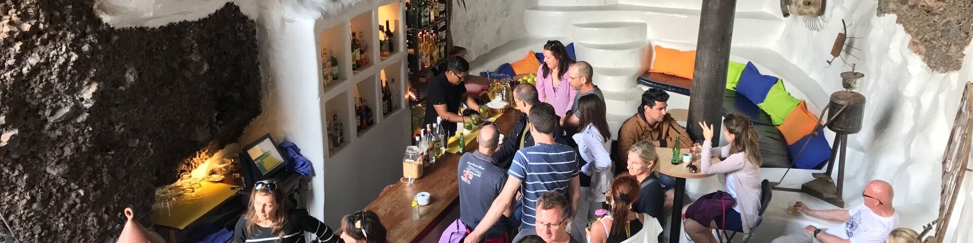 A cave bar with a rustic interior, a bar counter, and a seating area with cushions.