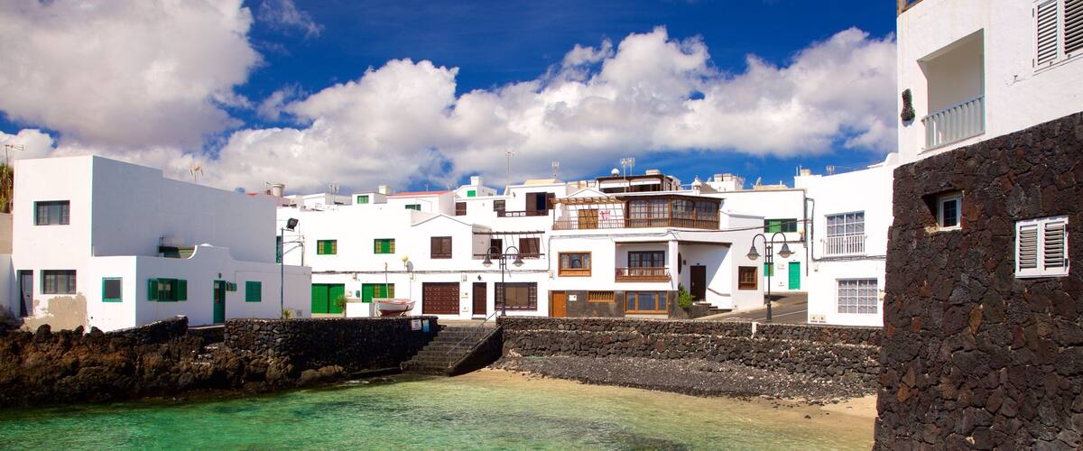 A coastal village with white buildings, clear turquoise waters, and a stone wall.