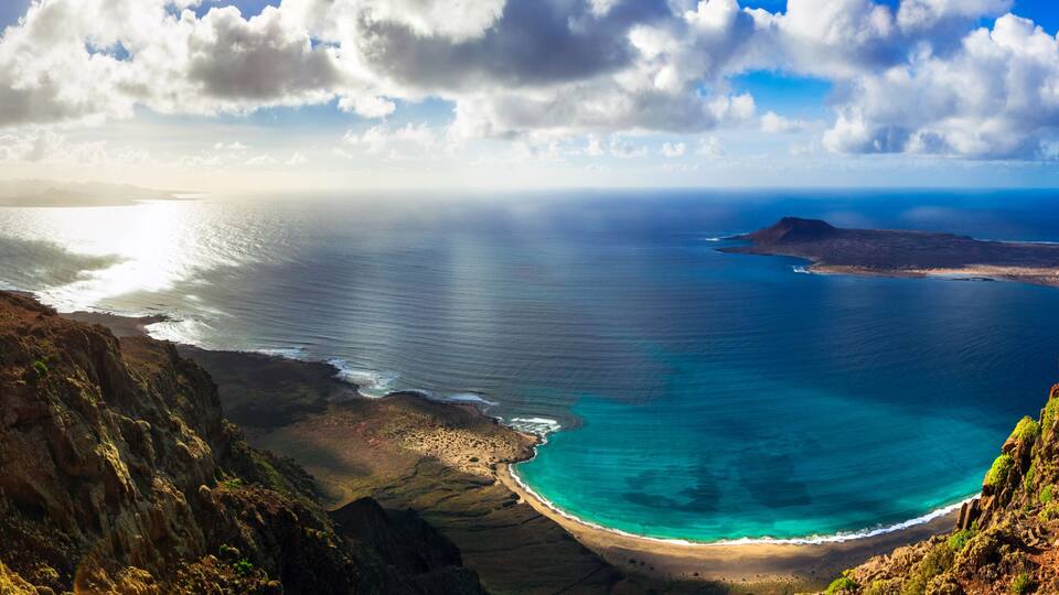 A coastal landscape with a clear view of the ocean, a sandy beach, and surrounding cliffs.