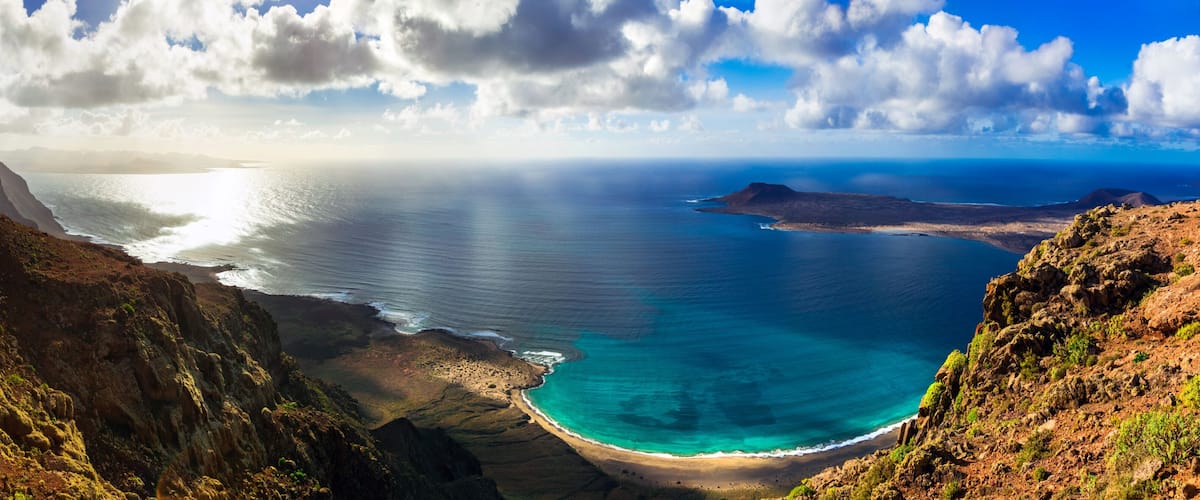 A coastal landscape with a clear view of the ocean, a sandy beach, and surrounding cliffs.