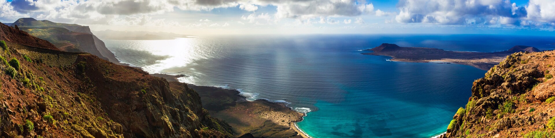 A coastal landscape with a clear view of the ocean, a sandy beach, and surrounding cliffs.