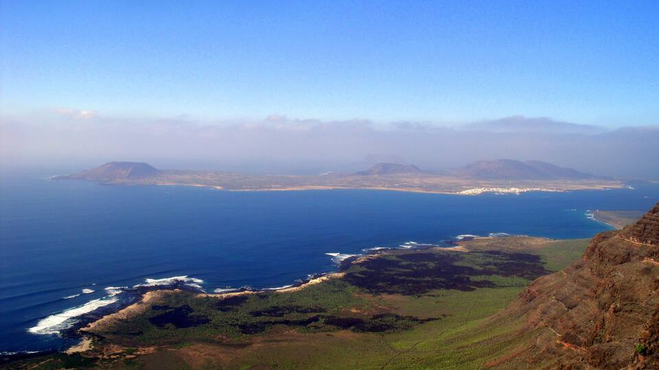 A coastal landscape with a clear view of the ocean, sandy beaches, and green hills.