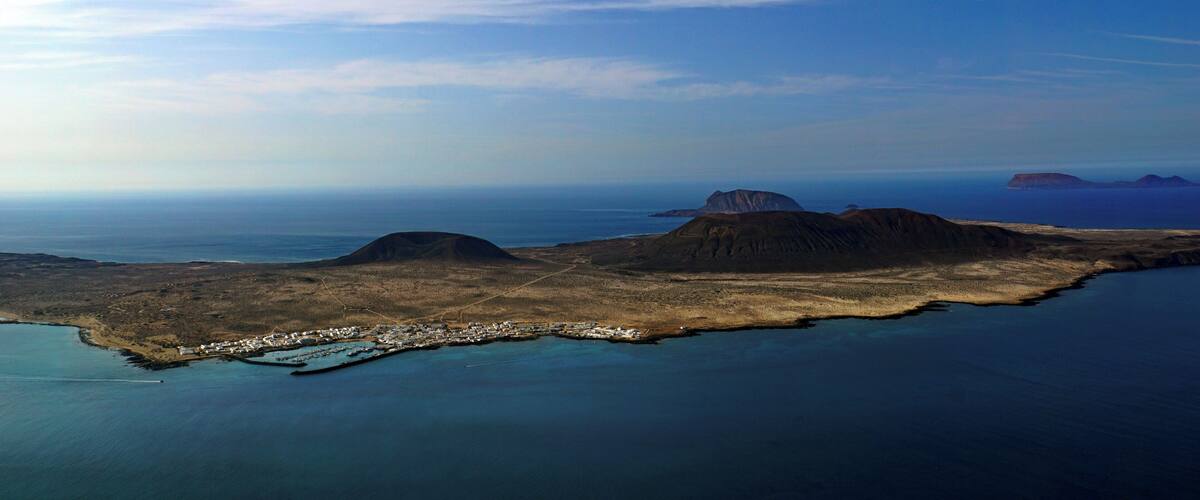 An aerial view of a coastal landscape with a small settlement near the water, surrounded by hills and a clear sky.