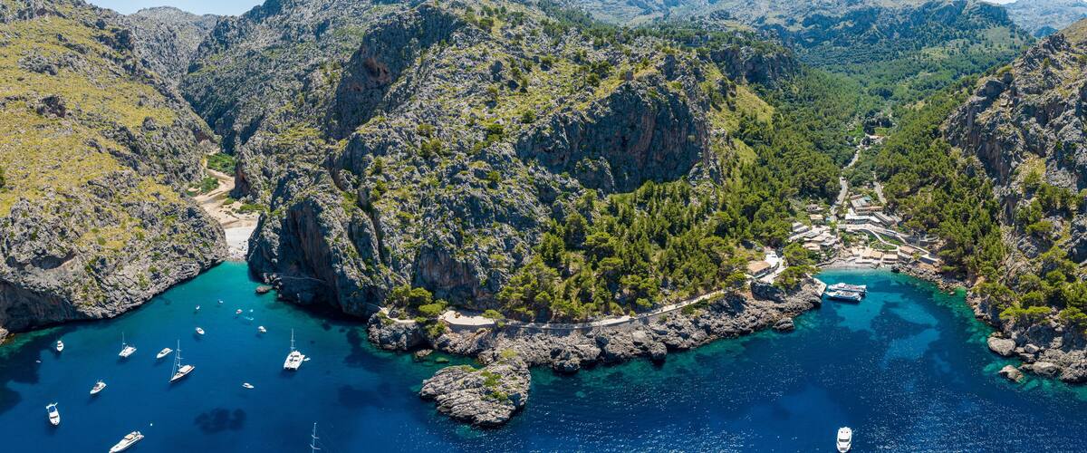 A coastal landscape with rocky cliffs, clear turquoise waters, and boats anchored near the shore.