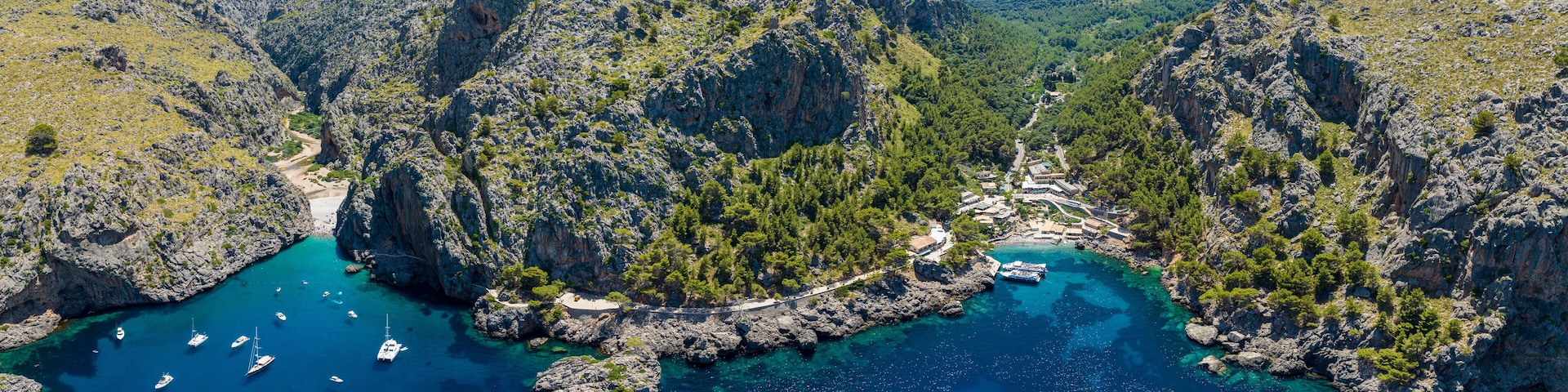 A coastal landscape with rocky cliffs, clear turquoise waters, and boats anchored near the shore.