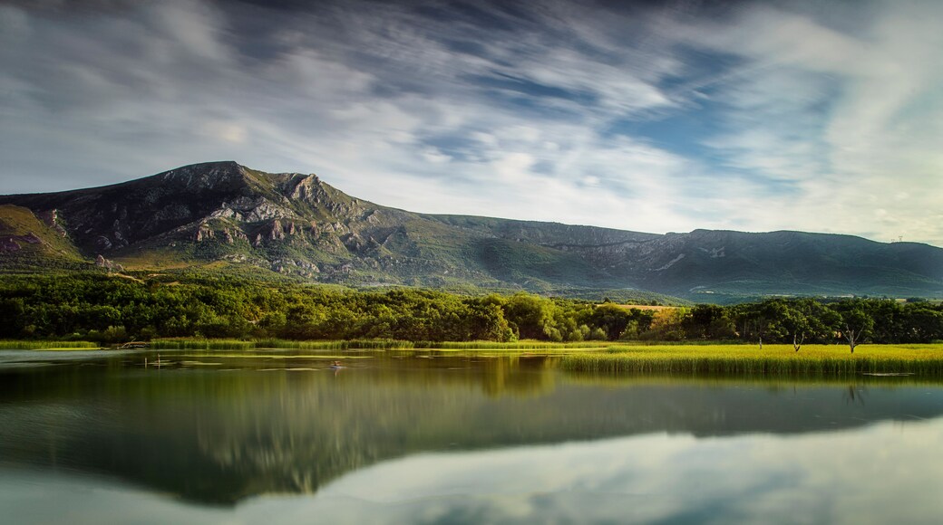 Scenic landscape of Sobron reservoir featuring mountain reflections in the calm water with green forests and a dramatic sky in northern Spain