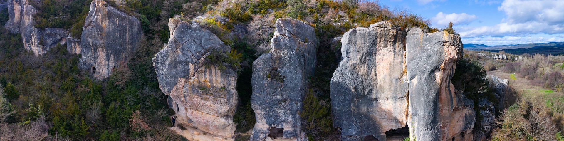 A rugged landscape with prominent rock formations and a narrow path leading through a forested area.