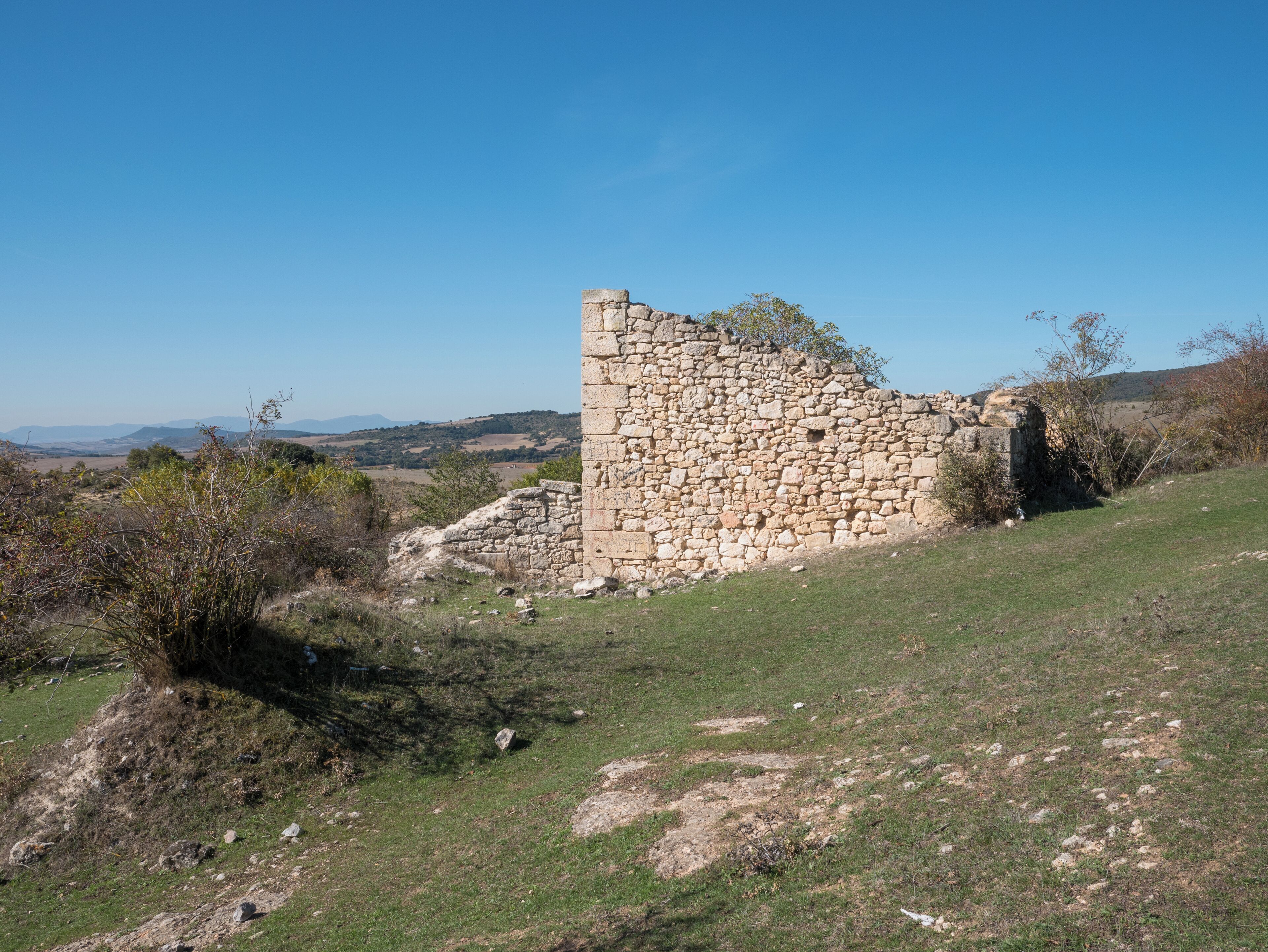 A stone ruin on a hillside with a clear sky.