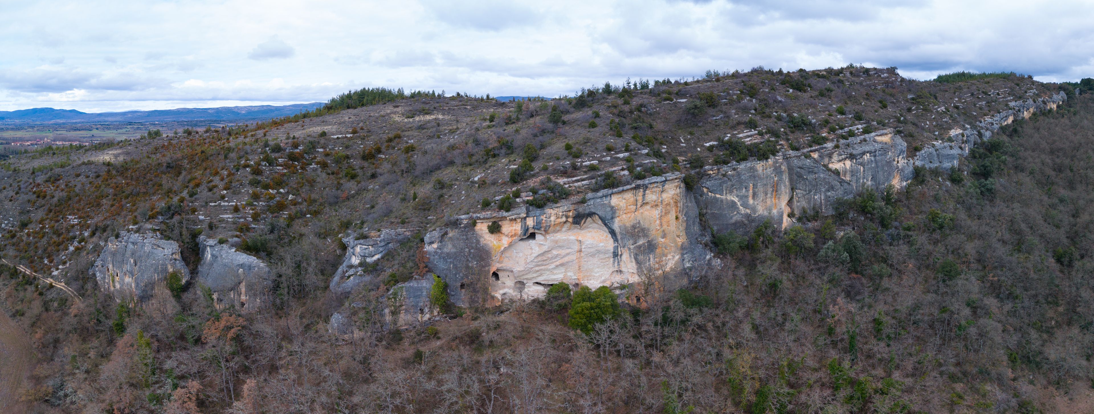 Un paysage montagneux accidenté, dominé par une formation rocheuse remarquable, qui présente une entrée de grotte.