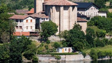 A historic church with a bell tower, surrounded by lush greenery and a calm lake.