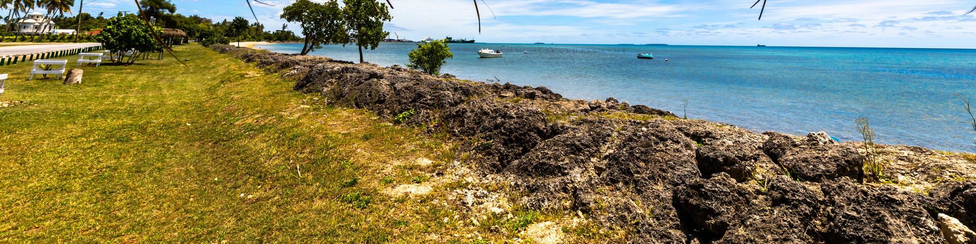 A beautiful view of the Tonga coastline taken from under a native hut on a perfect sunny day with deep blue sky and white clouds.