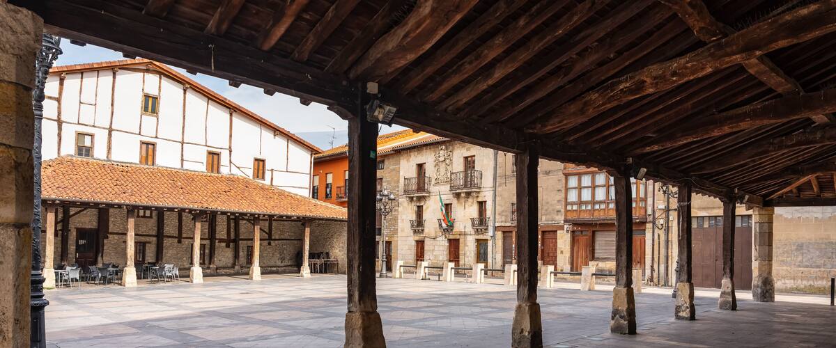 A covered courtyard with stone columns, tiled flooring, and traditional buildings with balconies.