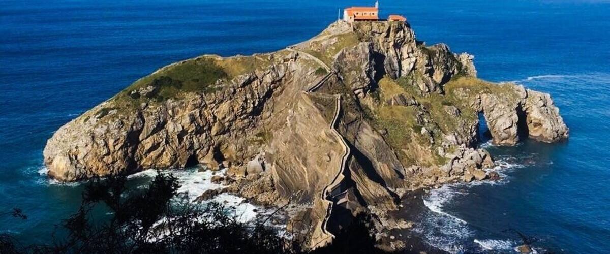 A rocky island with a lighthouse and a building on top, surrounded by the ocean.