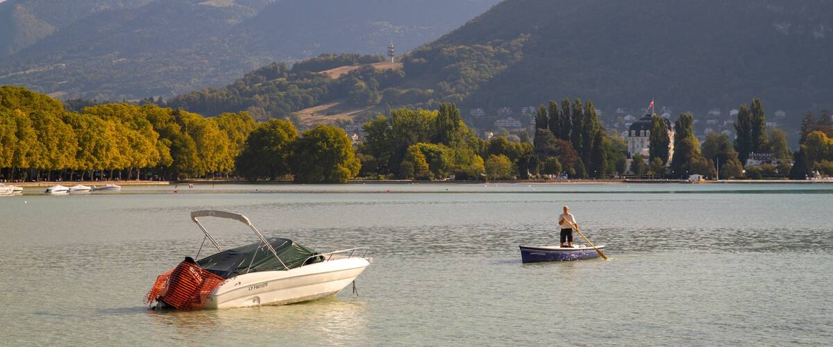 Ein See mit Booten, eine Person rudert, und Berge im Hintergrund.