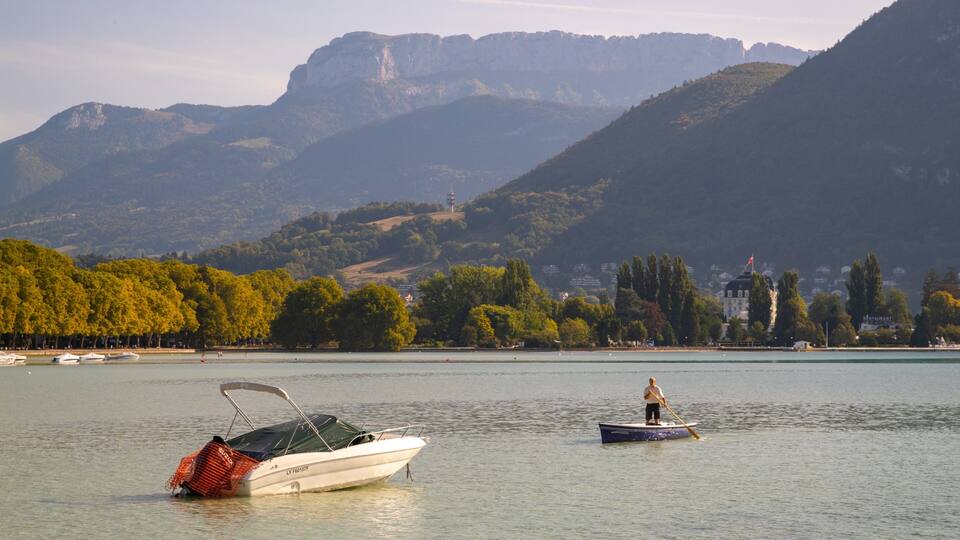 A lake with boats, a person rowing, and mountains in the background.