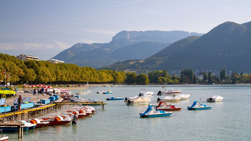 A lakeside with boats docked along the pier, surrounded by mountains and trees.