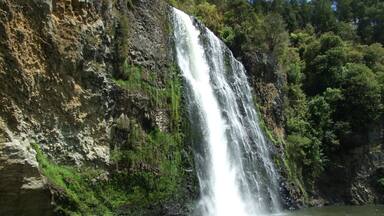 A waterfall cascading down a rocky cliff into a river surrounded by lush greenery.