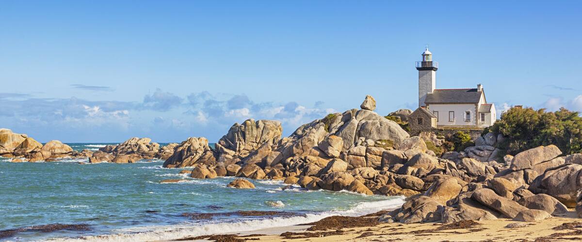 A rocky coastline with a lighthouse and a white building.