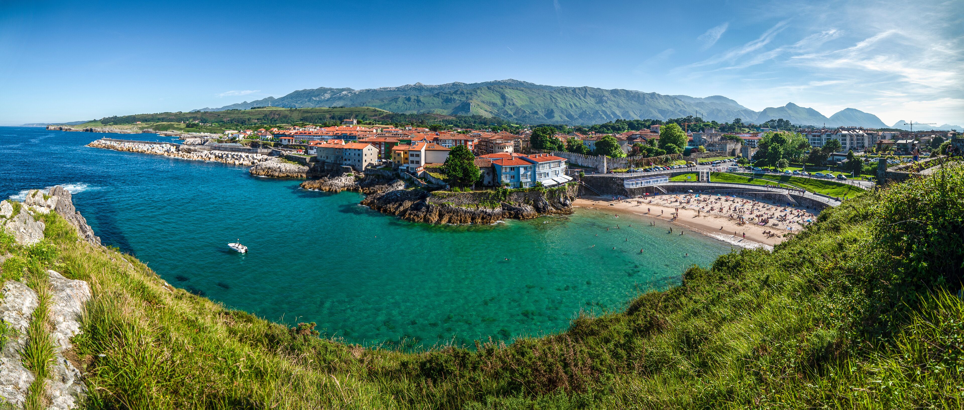 A coastal town with clear turquoise waters, a rocky shoreline, and a mountainous backdrop.