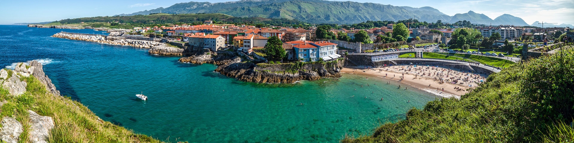 A coastal town with clear turquoise waters, a rocky shoreline, and a mountainous backdrop.