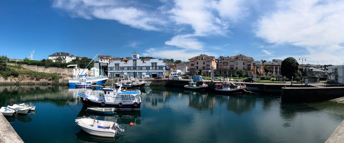 A harbor with boats docked, a stone wall, and buildings along the waterfront.