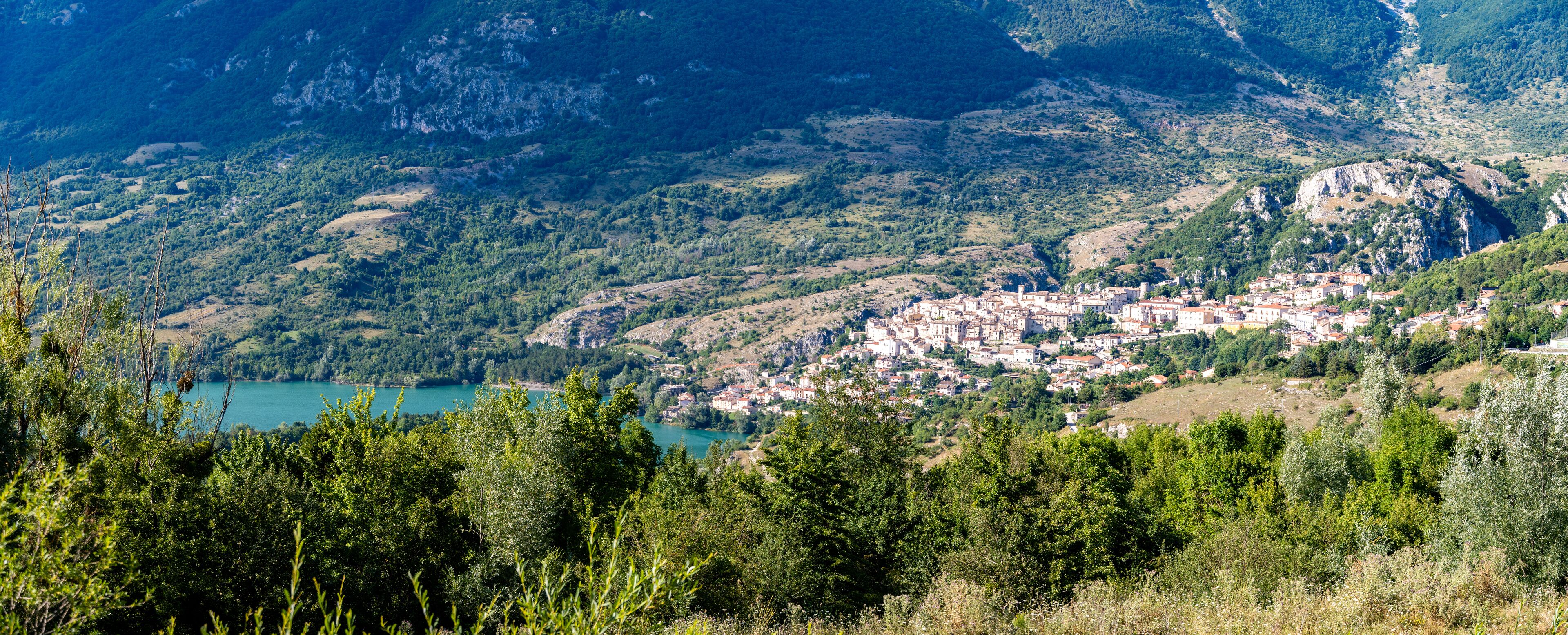 A mountainous landscape with a town nestled in the valley, surrounded by dense forests and a lake.