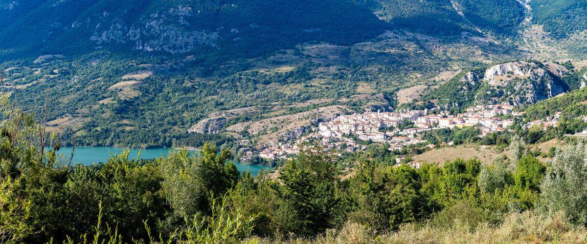 A mountainous landscape with a town nestled in the valley, surrounded by dense forests and a lake.