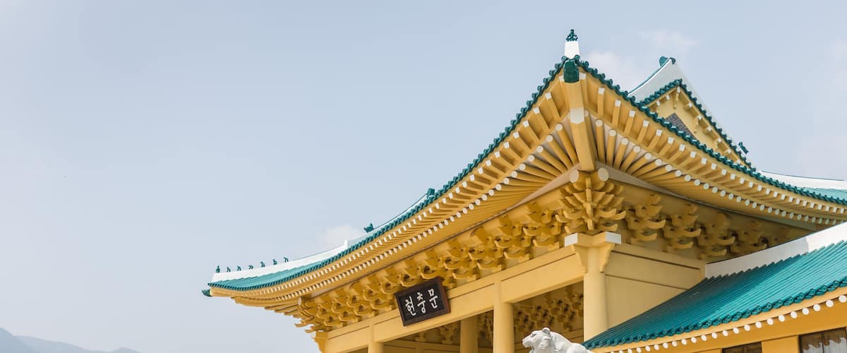 A traditional building with a yellow roof and green eaves, a stone lion statue, and a sign with Chinese characters.