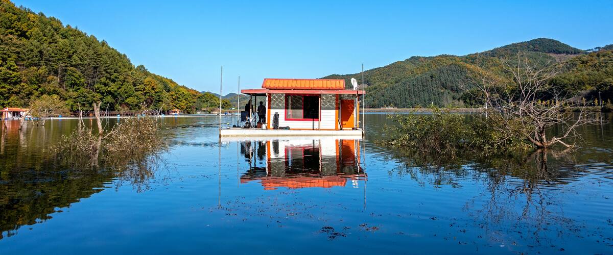 A houseboat on a calm lake surrounded by lush greenery and hills.