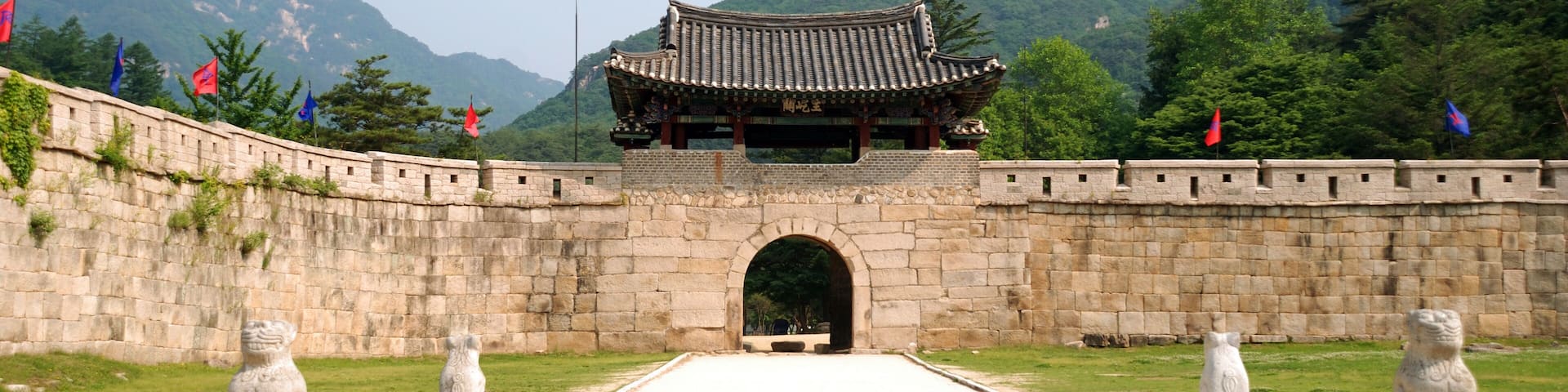 A traditional gate with a tiled roof, flanked by stone lion statues, leading to a mountainous landscape.