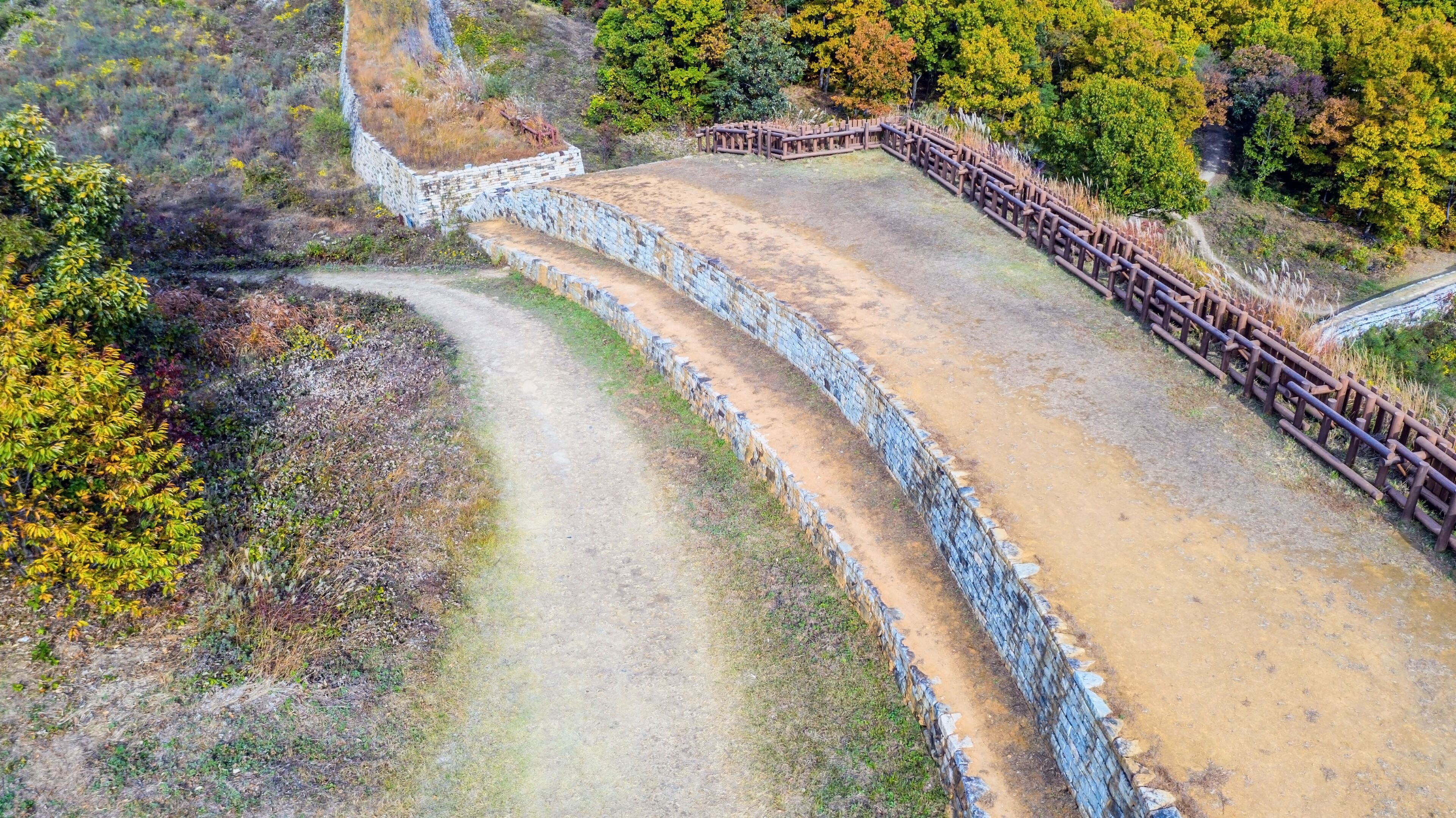 A winding dirt path with stone walls and wooden fences.